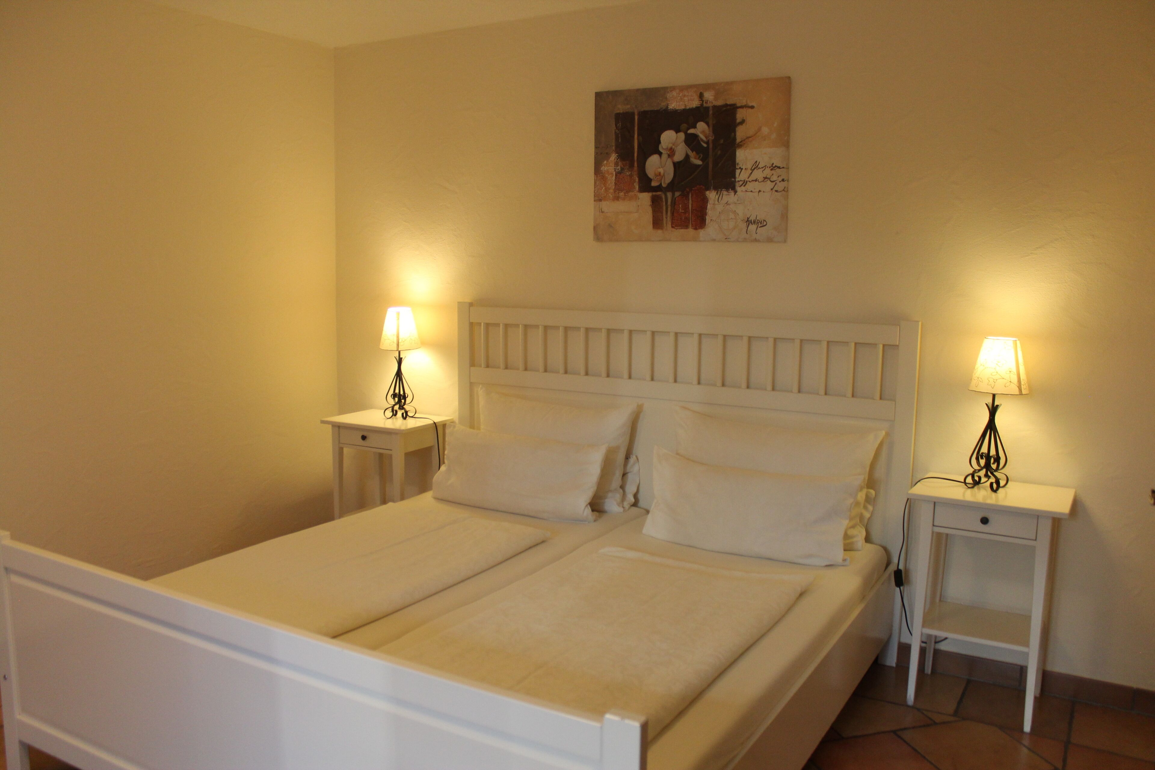 A double bed with white bedding, two bedside tables with lamps, and a wall-mounted artwork.