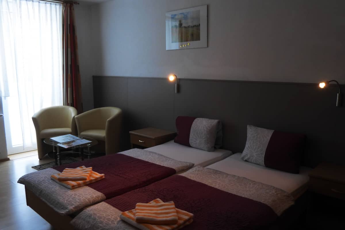 A hotel room with two beds, a chair, a small table, and a nightstand.