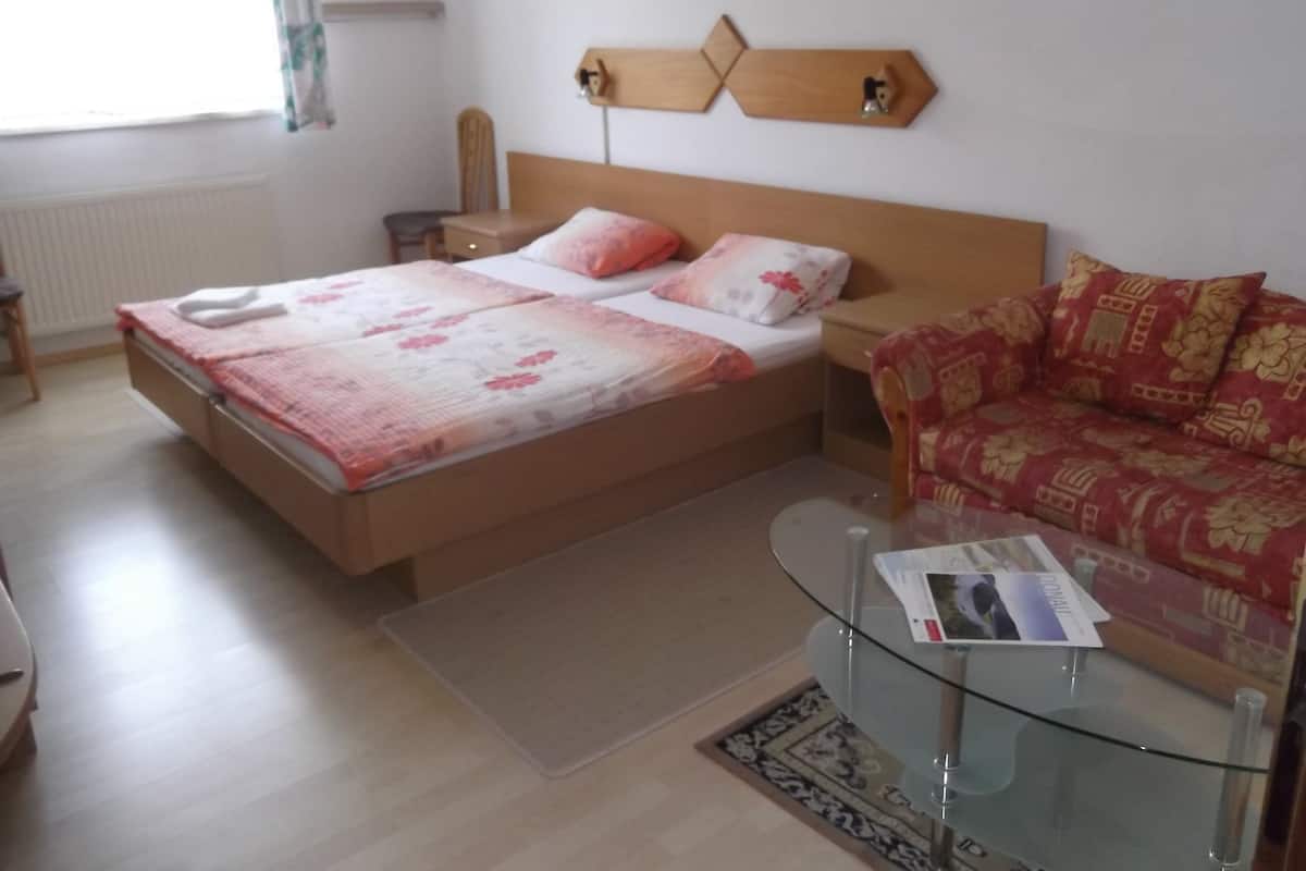 A bedroom with two beds, a sofa, a glass coffee table, and a wall-mounted shelf with decorative items.