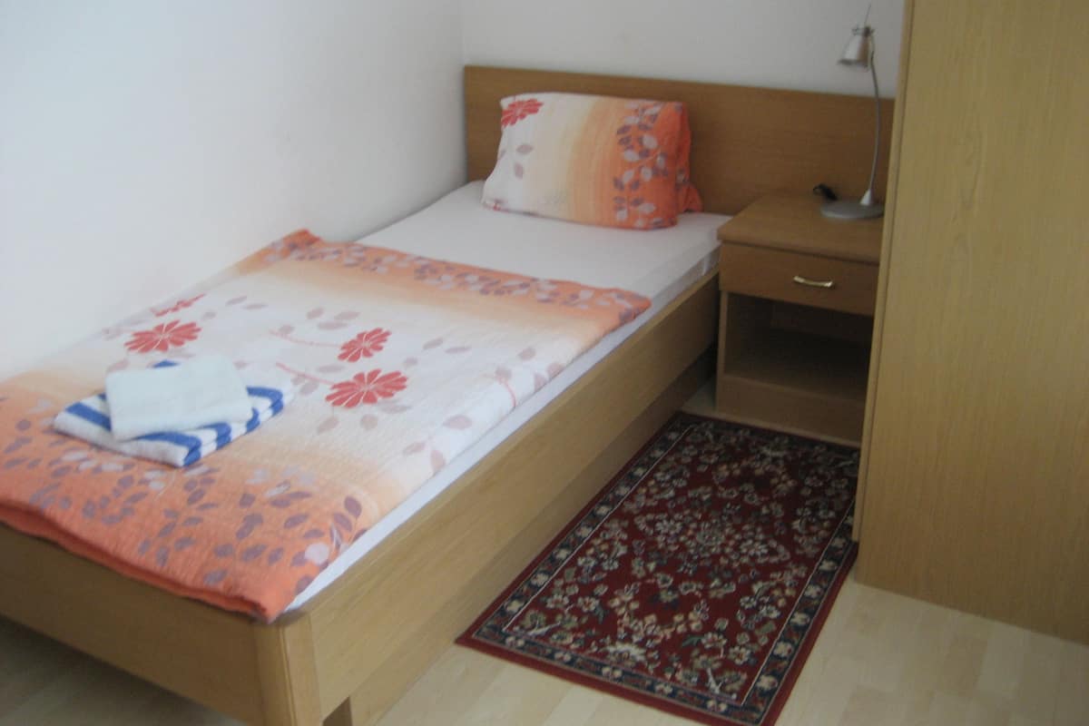 A single bed with a floral bedspread, a nightstand, and a red patterned rug.
