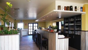 Restaurante com balcão comprido, cadeiras pretas e área de bar com prateleiras cheias de garrafas.
