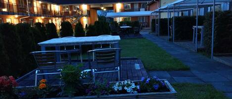 An outdoor patio area with a table and chairs, surrounded by potted plants and a well-maintained lawn.