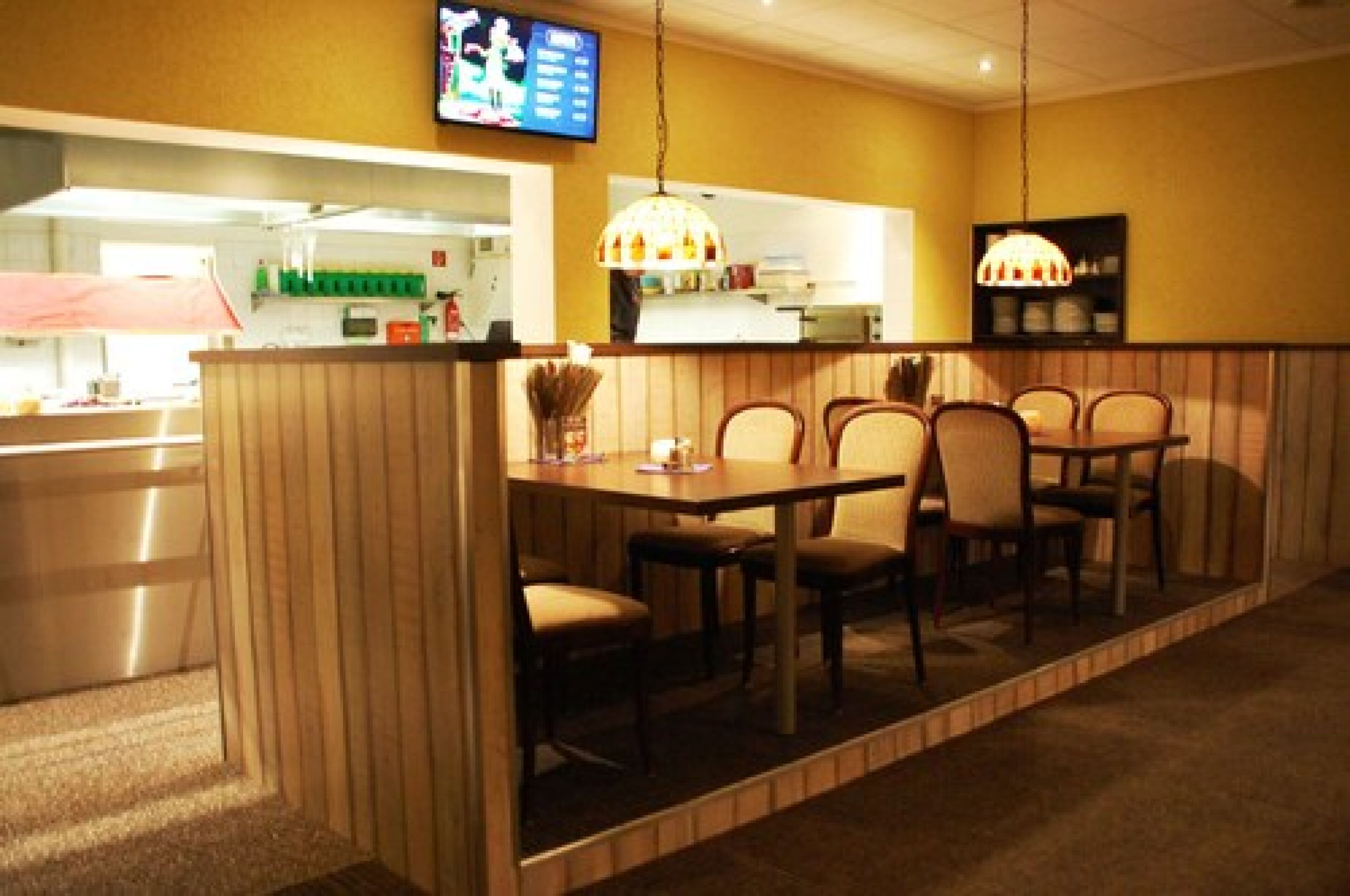 A restaurant with a booth seating area, a counter with a menu, and a television mounted on the wall.