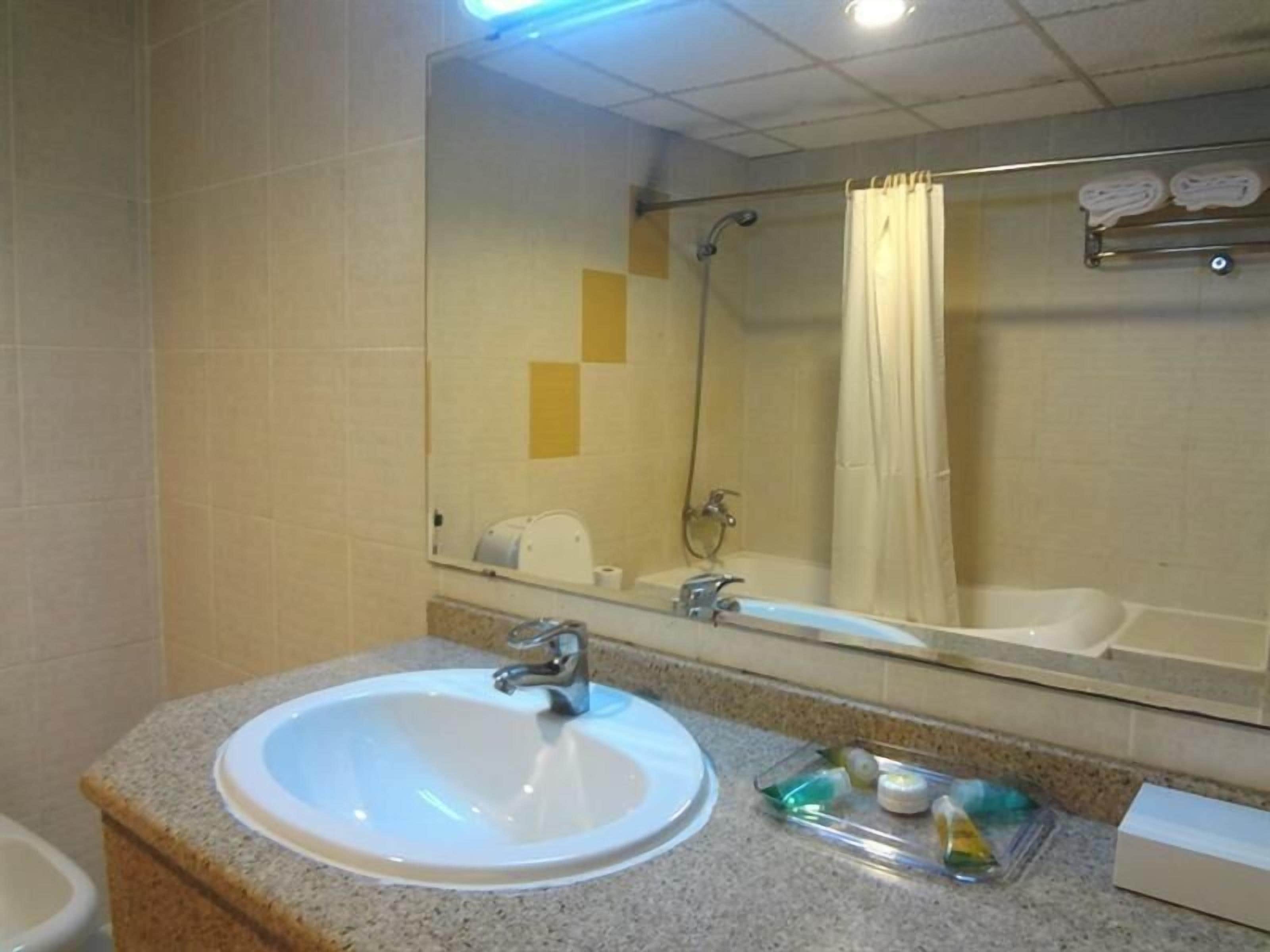 A bathroom with a sink, mirror, shower, and towel rack.