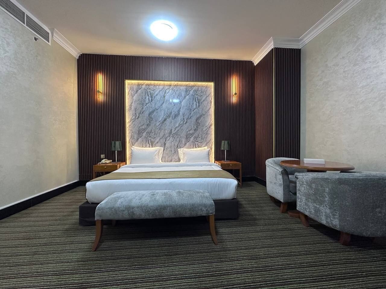 Una habitación de hotel con una cama grande, dos mesitas de noche, un escritorio y una silla.
