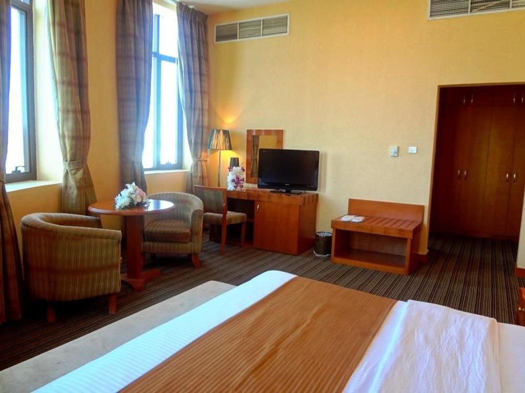 A hotel room with a bed, a desk with a television, a chair, a lamp, and a wardrobe.