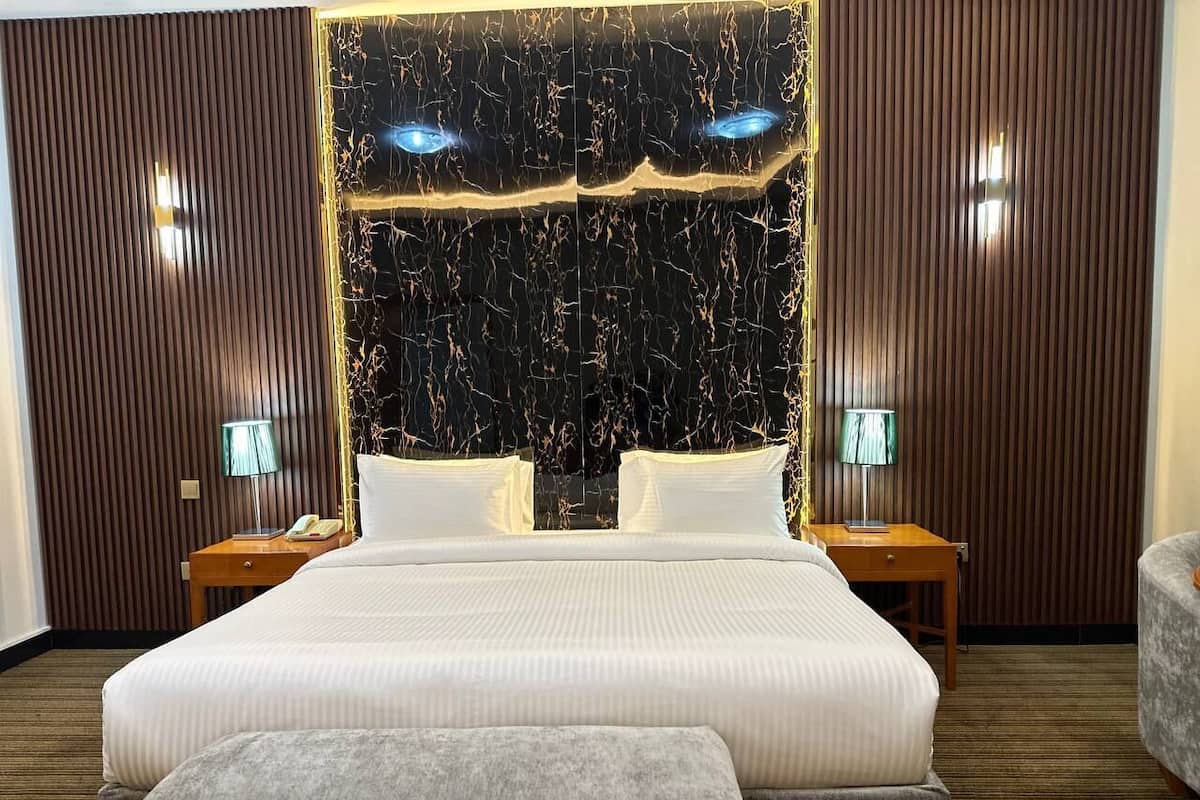 A large bed with white linens, two bedside tables with lamps, and a bench at the foot of the bed.