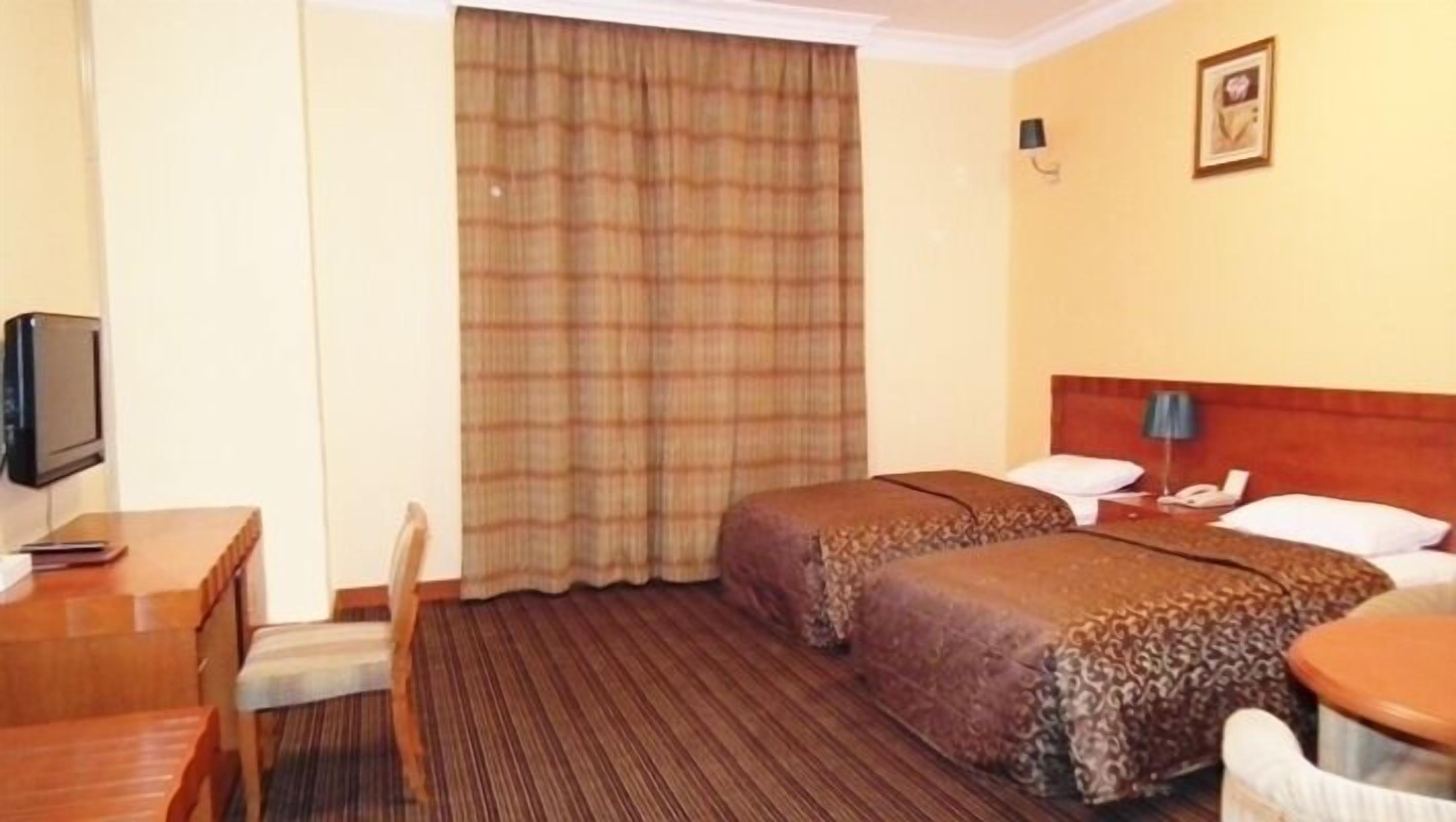 Habitación de hotel con dos camas, un escritorio, una silla, un televisor y una ventana con cortinas.