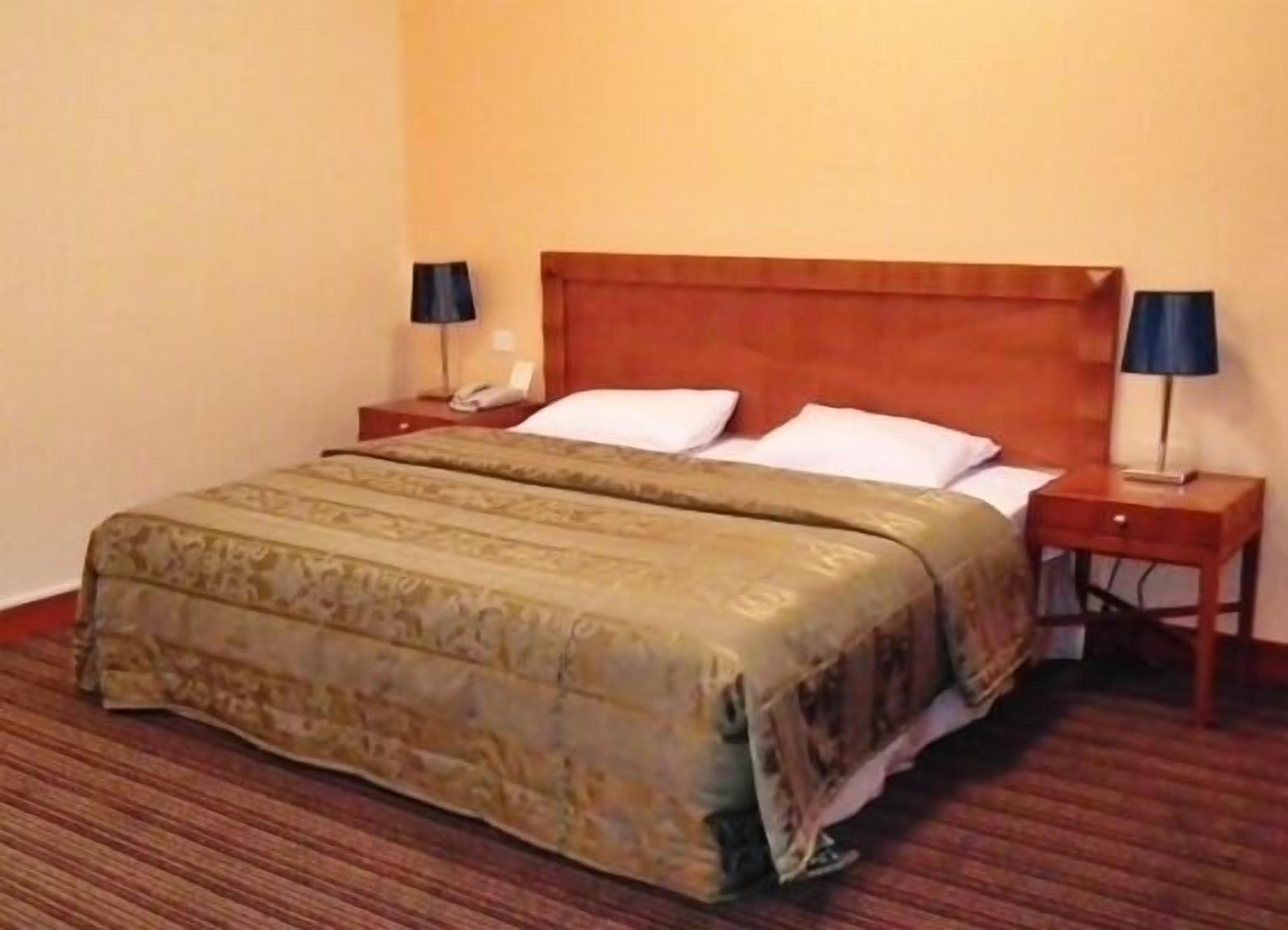 A hotel room with a double bed, two bedside tables, and two lamps.