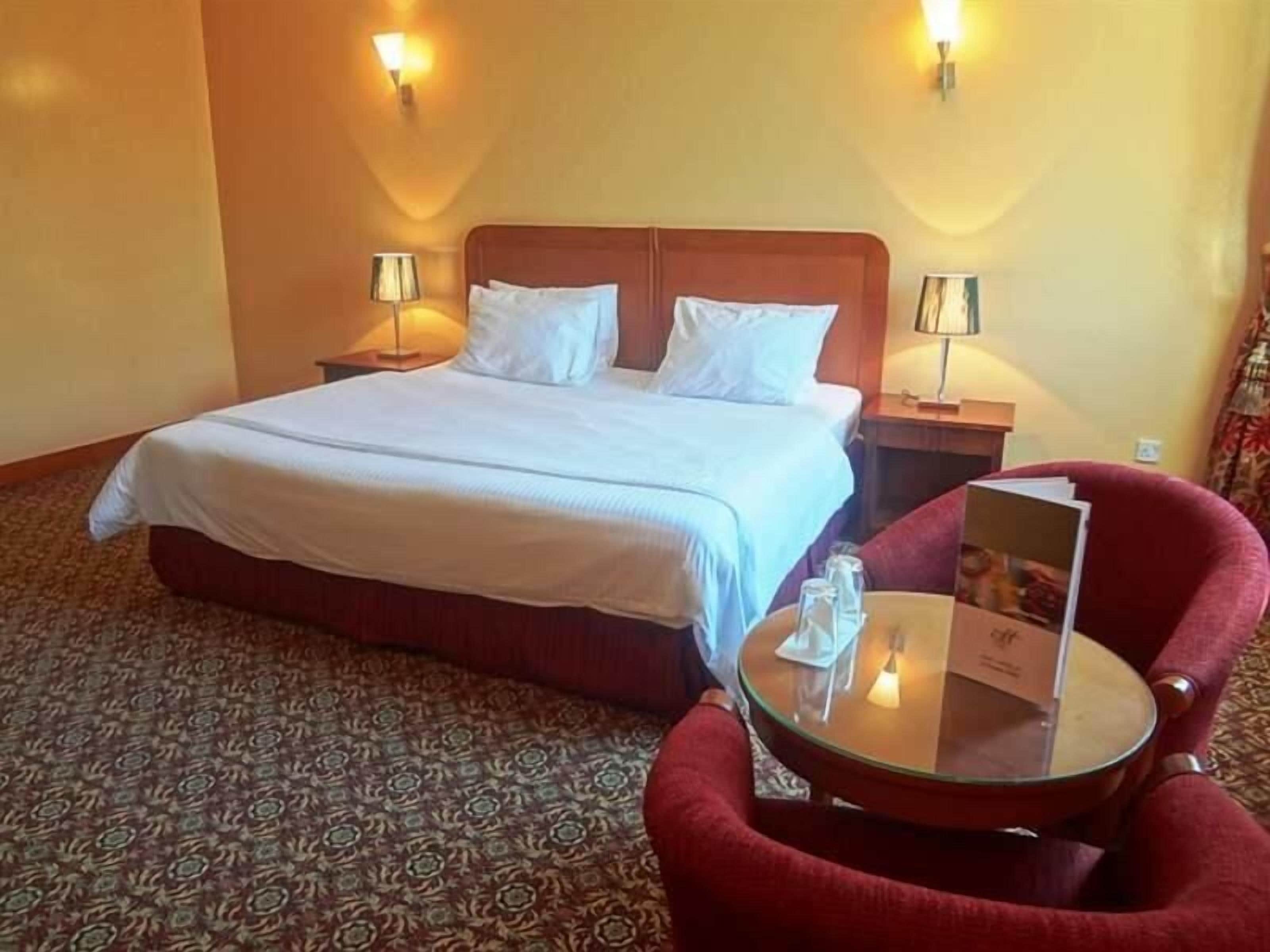A hotel room with a large bed, two bedside lamps, a round table with a menu, and a red chair.