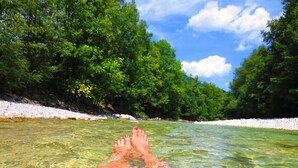 Ein klarer Fluss mit den Beinen einer Person im Wasser, umgeben von üppigen grünen Bäumen und einem weißen Sandufer.