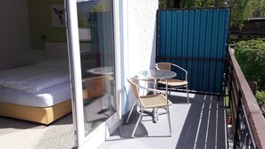 A balcony with a bed, two wicker chairs, a small round table, and a blue-striped fence. - Hotel Oase (Bad Ischl)