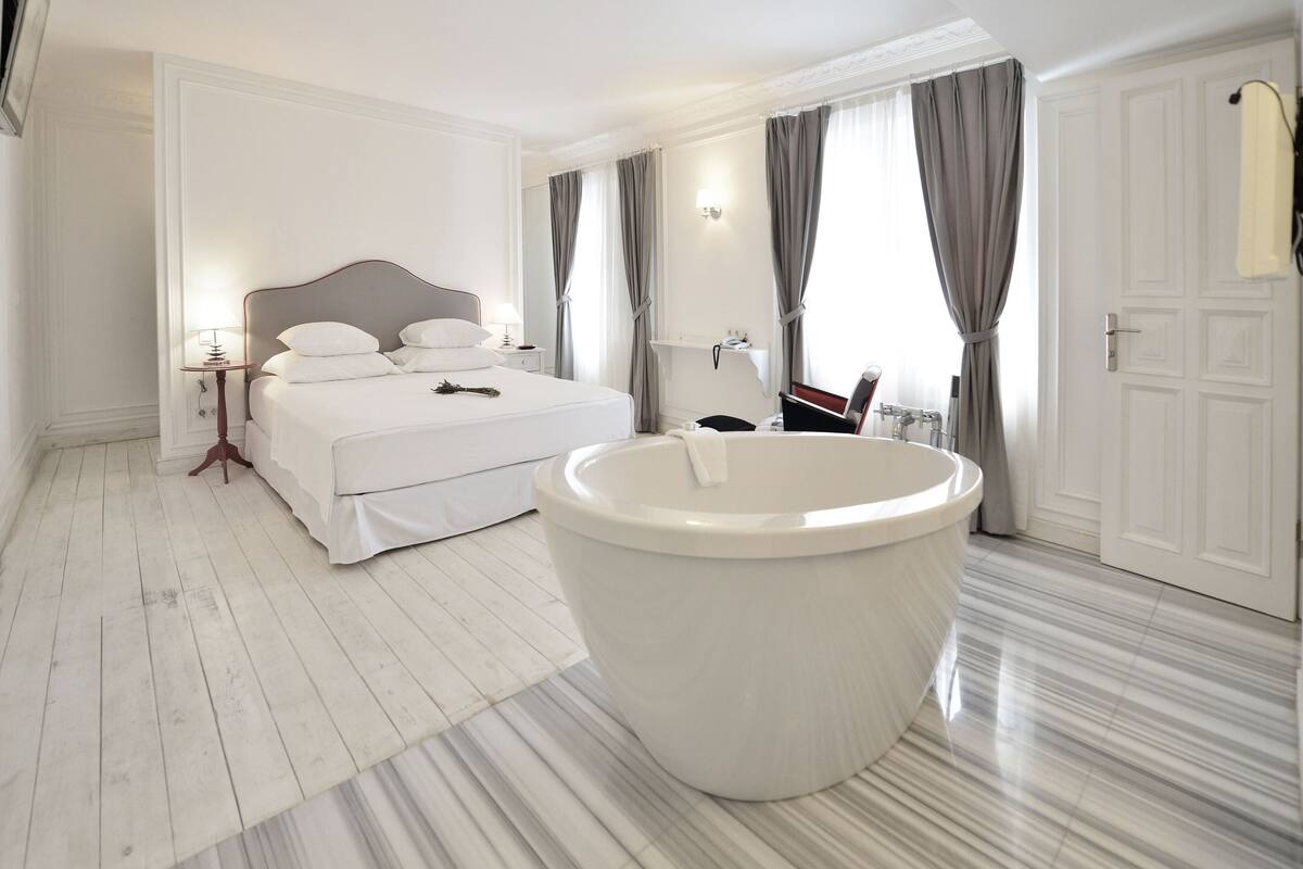 Une chambre d’hôtel moderne avec un grand lit, une baignoire et un sol en marbre.