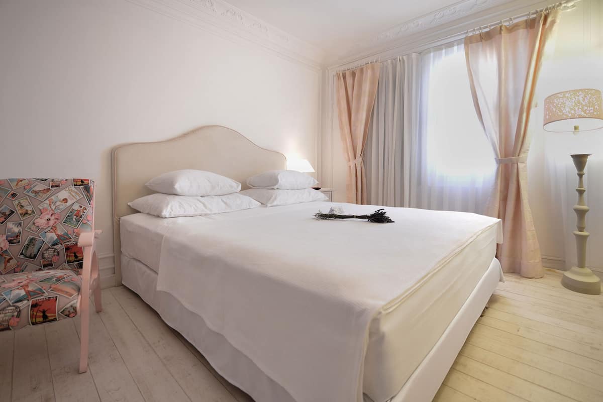 Un lit bien fait, avec du linge de lit blanc, une chaise décorative à motifs floraux et un grand lampadaire.