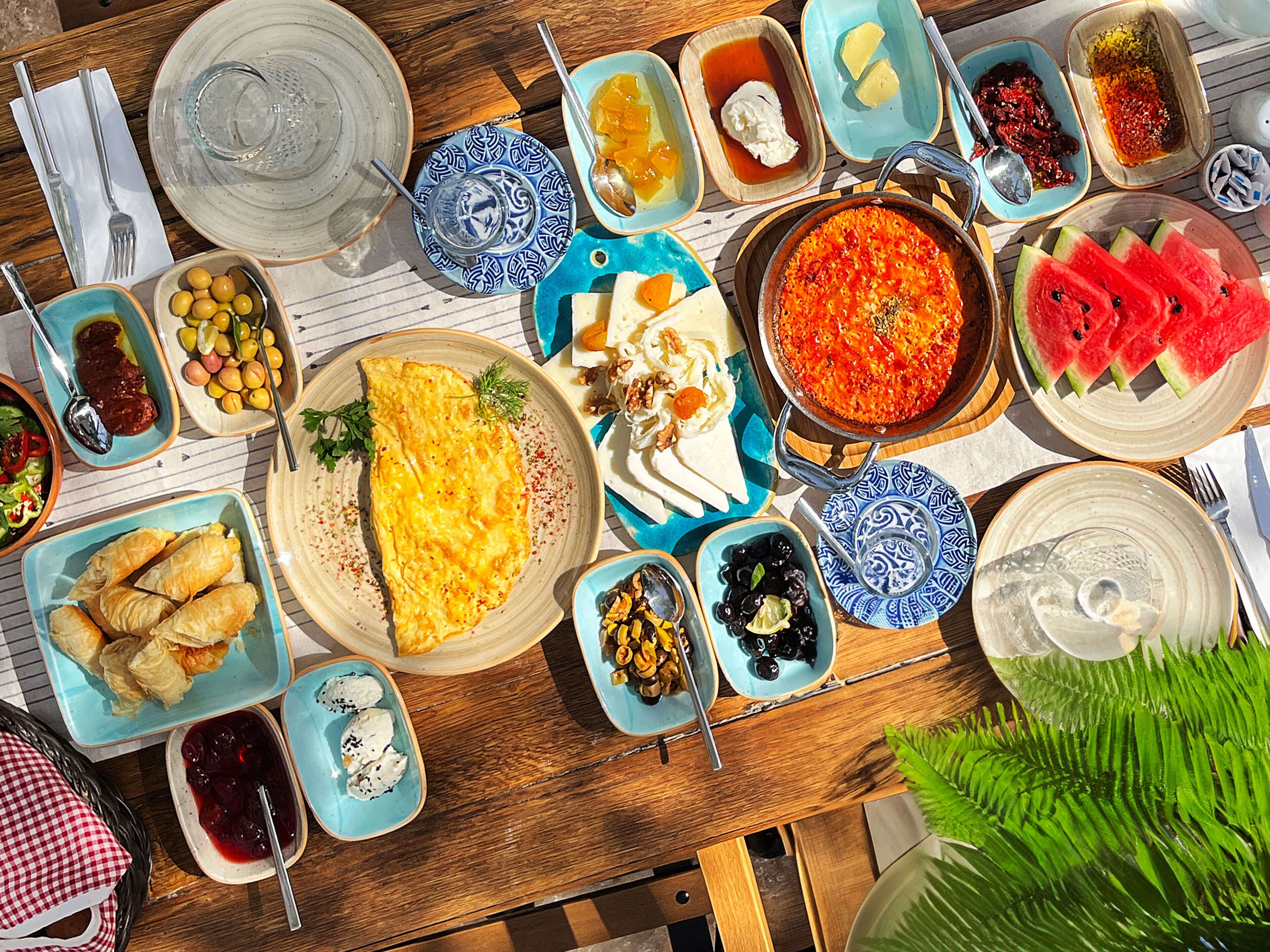A wooden table with various dishes including an omelette, watermelon slices, and several small bowls of food.