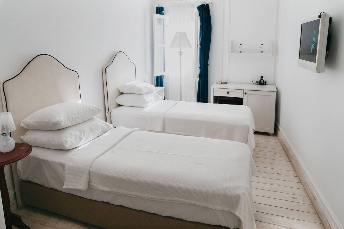 Une chambre avec deux lits, une table de chevet avec une lampe, un petit bureau et un téléviseur fixé au mur.