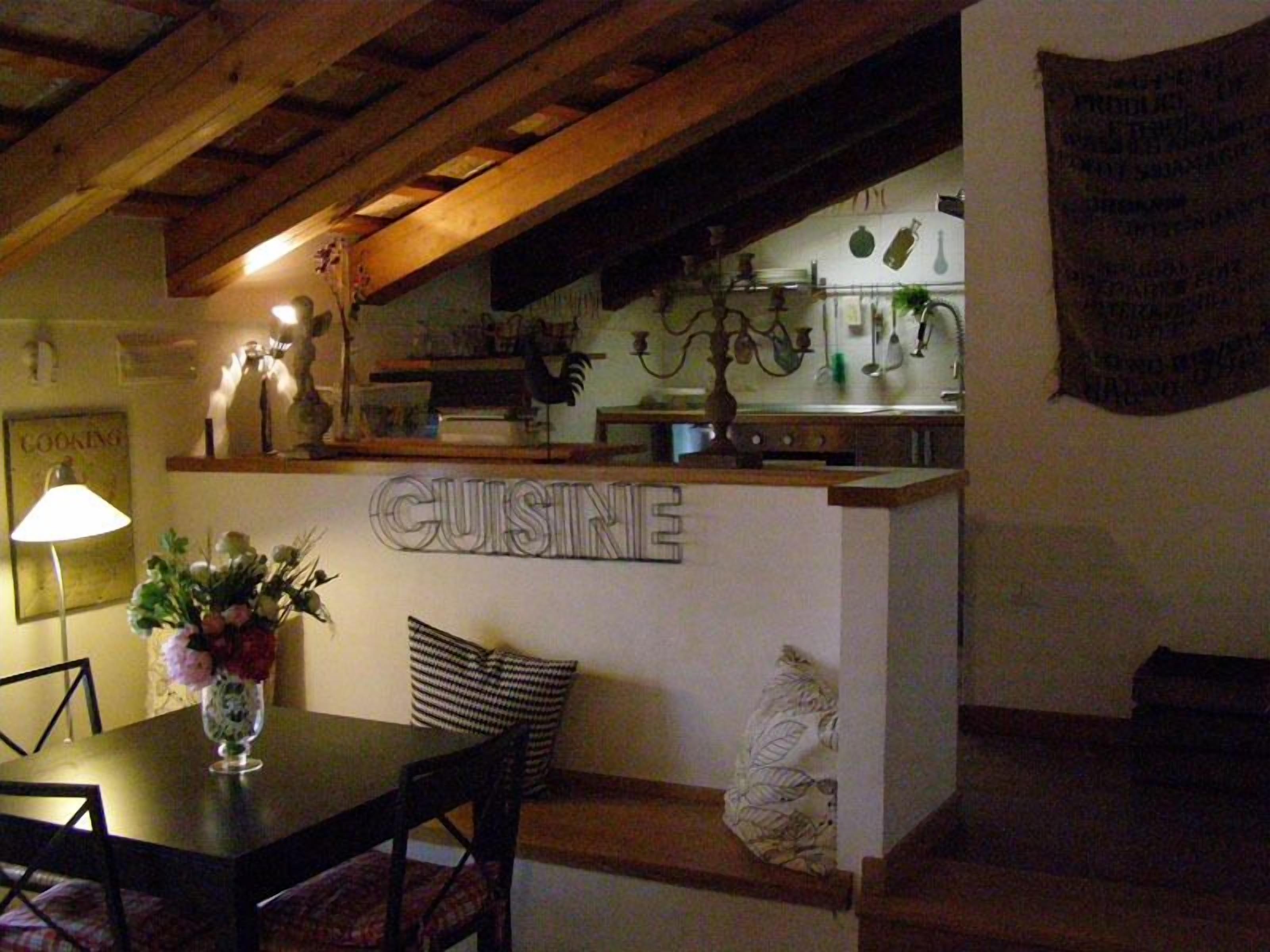 A cozy kitchen with wooden beams, a dining table with chairs, and a sign that reads "CUISINE".
