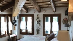 A rustic bedroom with exposed wooden beams, a large bed with floral bedding, and a vintage lamp. - Locanda San Tomaso (Treviso)