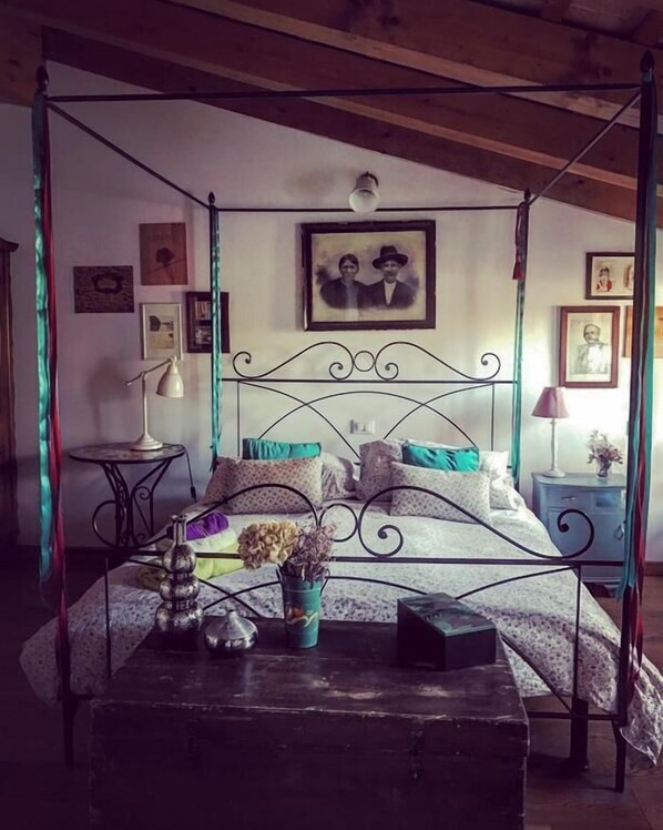 A four-poster bed with a metal frame, a small table with a lamp, and a vase with flowers. - Locanda San Tomaso (Treviso)