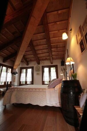 A cozy room with a wooden ceiling, a bed with a floral bedspread, a large barrel, and a lamp on a nightstand. - Locanda San Tomaso (Treviso)
