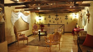 A room with wooden beams, a chandelier, and a fireplace. There are two ornate chairs and a table with a vase of flowers. - Morenica del Rosario (Cuenca)