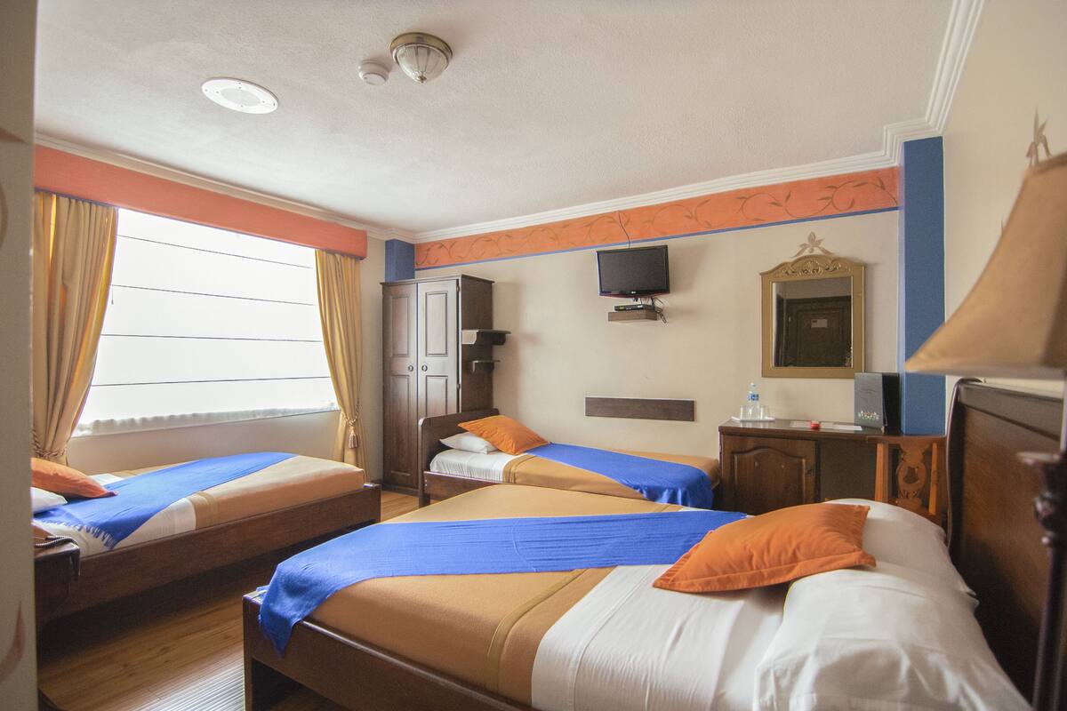 A hotel room with two beds, a television, a mirror, and a small desk.