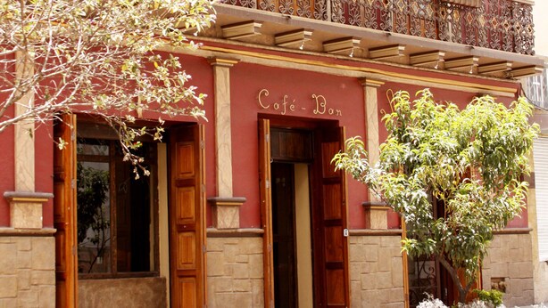 A building with a balcony, a sign reading "Café Bar", and flags. - Morenica del Rosario (Cuenca)