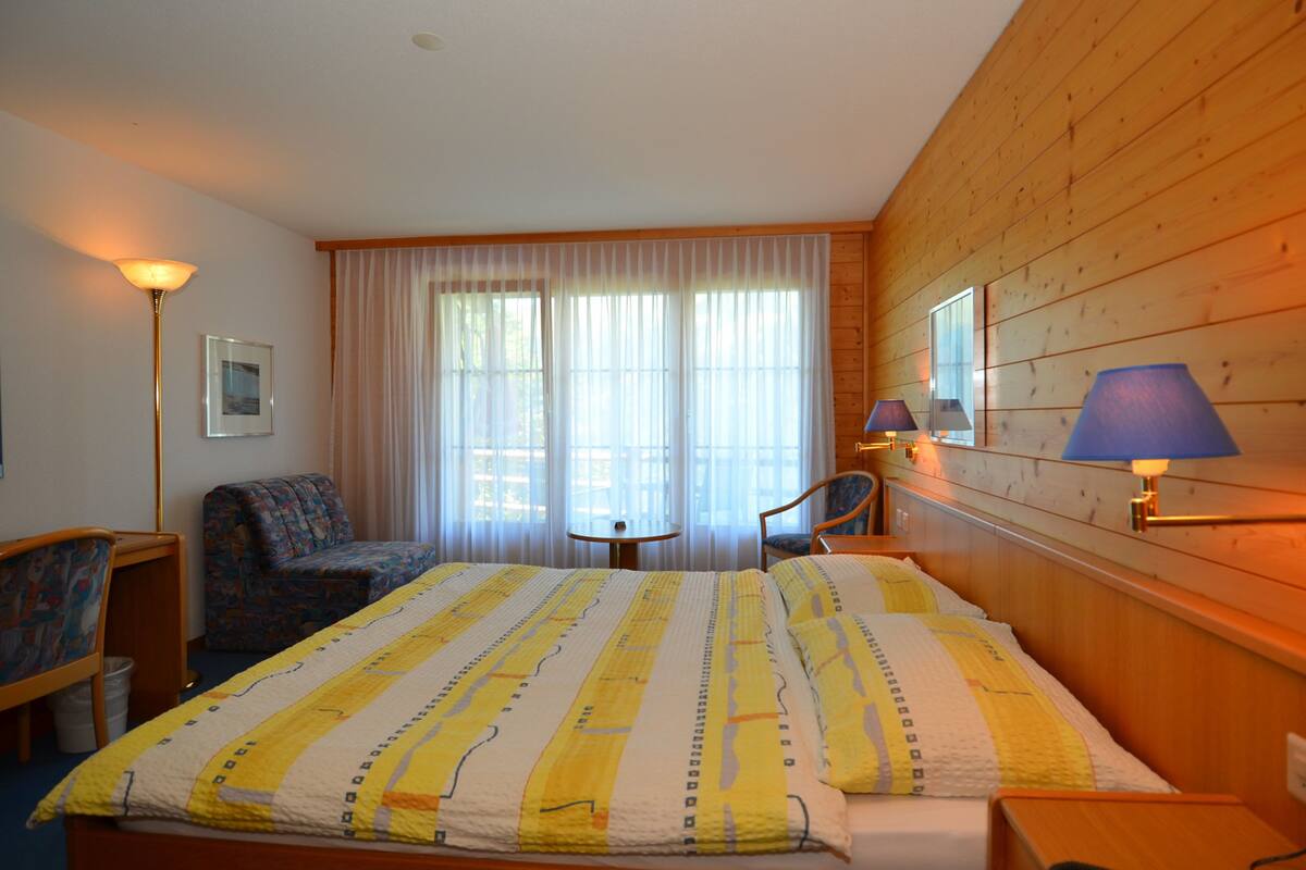 A hotel room with a large bed, a chair, a small table, and a lamp.