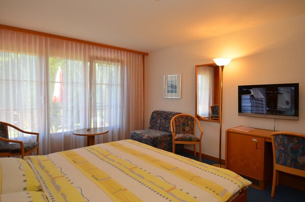 A hotel room with a bed, two chairs, a small table, a TV, and a mirror.
