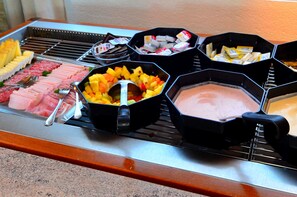 A buffet with various food items including meats, fruits, and beverages.