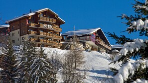 A multi-story hotel with a wooden facade, balconies, and a ski slope in the background.