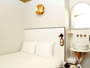 Experience comfort in this stylish room with a neatly made bed, wall-mounted light fixture, and modern bathroom amenities.