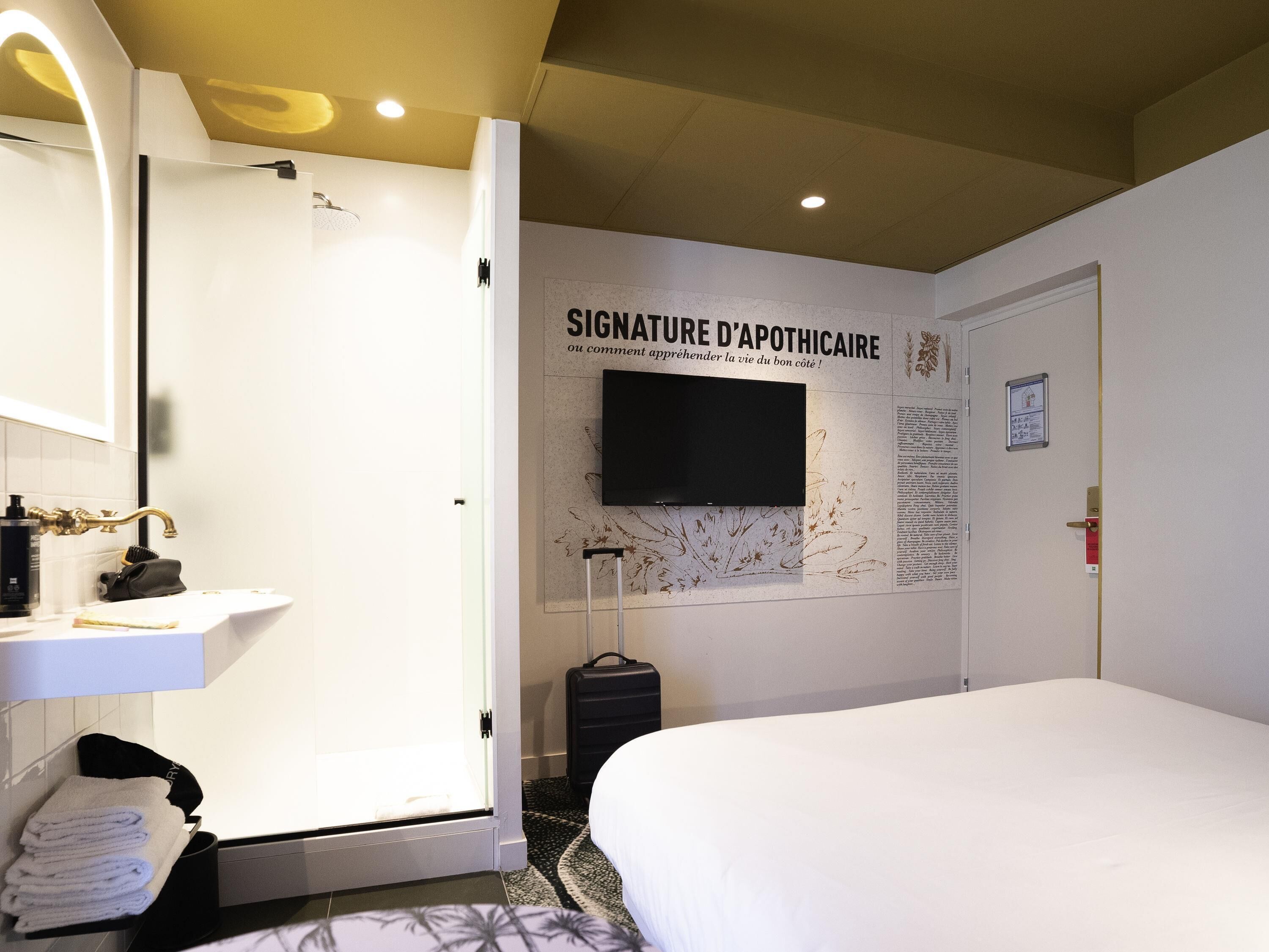 Una habitación de hotel con cama, baño con lavamanos y televisor montado en la pared.