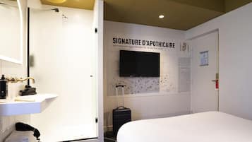 Una habitación de hotel con cama, baño con lavamanos y televisor montado en la pared.