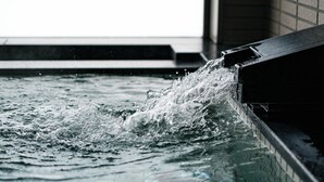 A pool with water splashing into it, surrounded by a tiled wall.