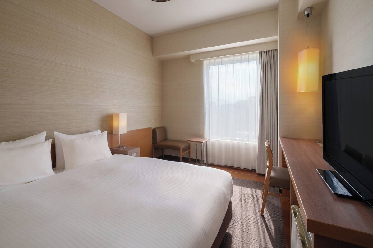 A hotel room with a large bed, a desk, a television, and a window with curtains.