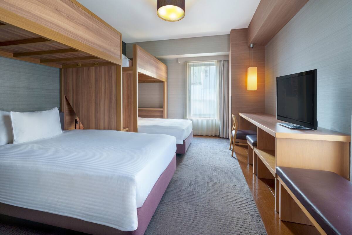 A hotel room with two beds, a TV, and a desk.