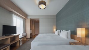 A modern hotel room with two large beds, a flat-screen TV, a desk, and a seating area.