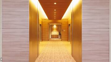 Un pasillo moderno con paneles de madera y suelo alfombrado, que conduce a una zona de recepción con mostrador y sillas.