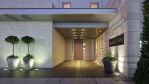 A hotel entrance with a tiled facade, a covered walkway, and potted plants.