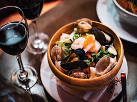 Un plato de mariscos en un cuenco de madera, acompañado de una copa de vino tinto.