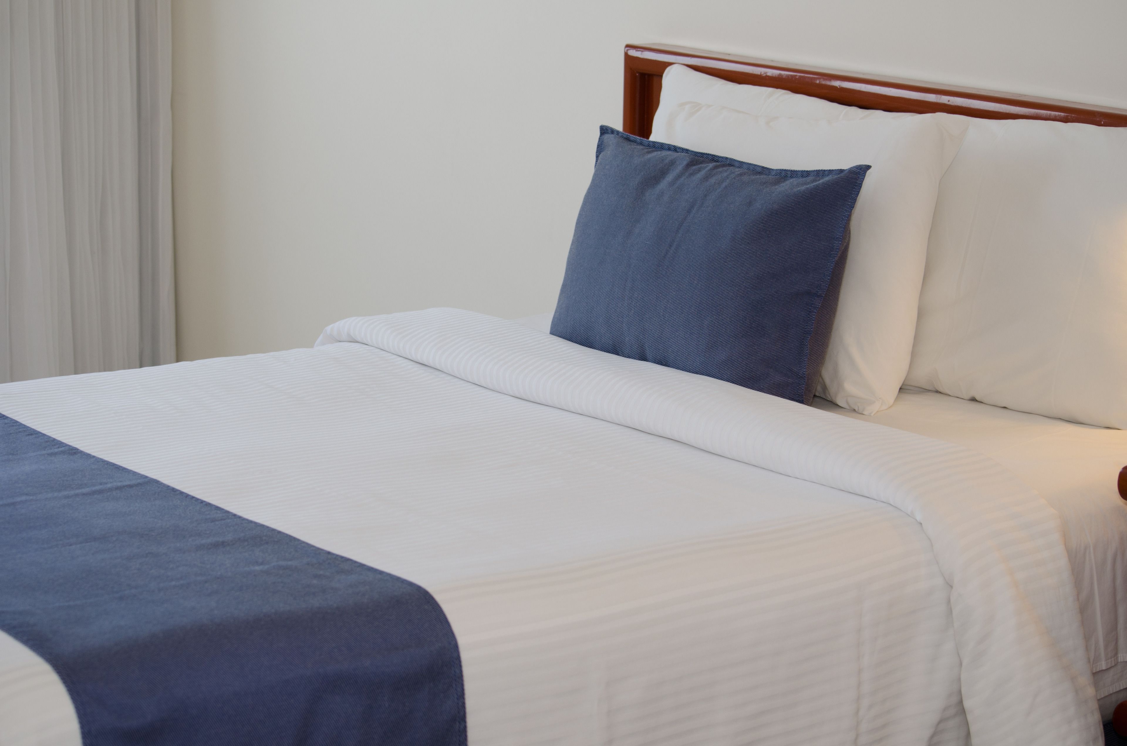 A neatly made bed with a blue and white bedspread, a wooden headboard, and white pillows.