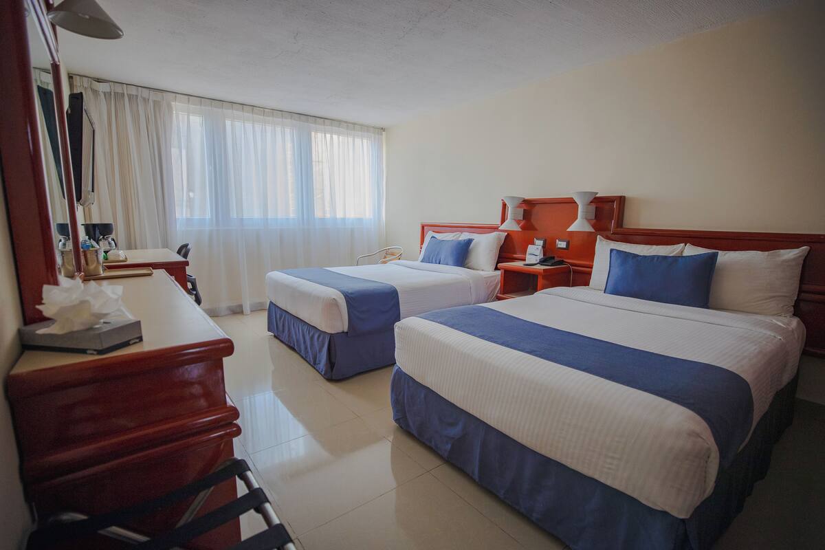 A hotel room with two beds, a desk, and a chair.