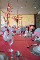 Un salón de banquetes con mesas dispuestas para un evento formal, con centros de mesa florales y manteles rojos.