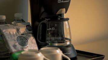 A coffee maker, a glass carafe, and a tray with cups and bottled water on a table.
