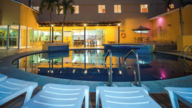 Un espace piscine avec des chaises longues, une petite piscine et, au fond, un bâtiment abritant un restaurant et un bar.