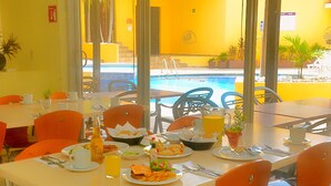 Un espace repas avec des tables préparées pour le petit-déjeuner, une vue sur la piscine et des sièges à l’extérieur.