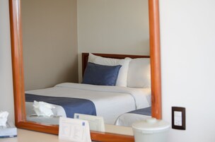 Una cama bien hecha con cabecera de madera, ropa de cama blanca y azul, y una mesita de noche con un dispenser de pañuelos y un objeto pequeño.