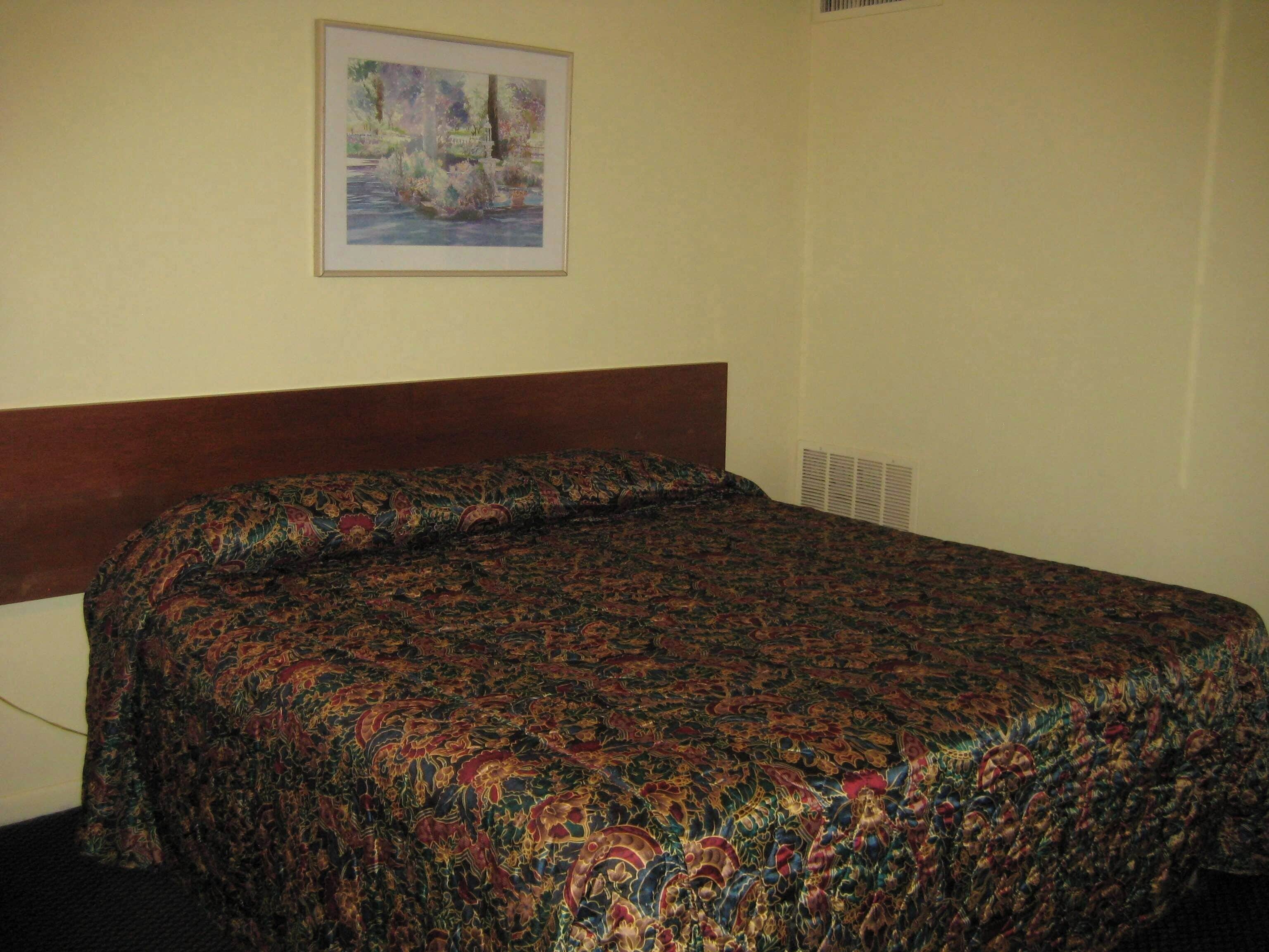A hotel room with a bed, a framed painting on the wall, and a window with blinds.