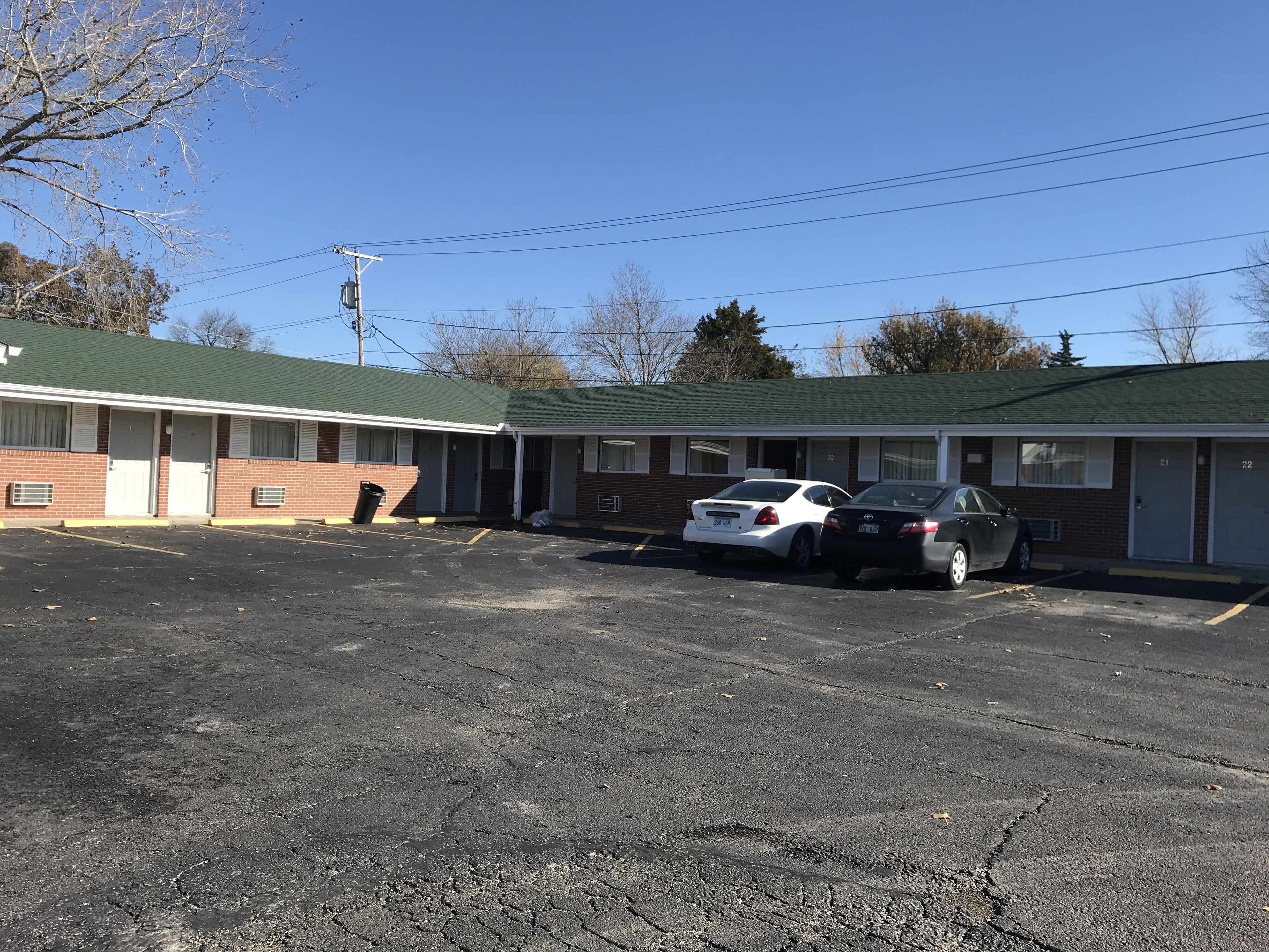 A motel with two cars parked in front, a brick exterior, and a green roof.